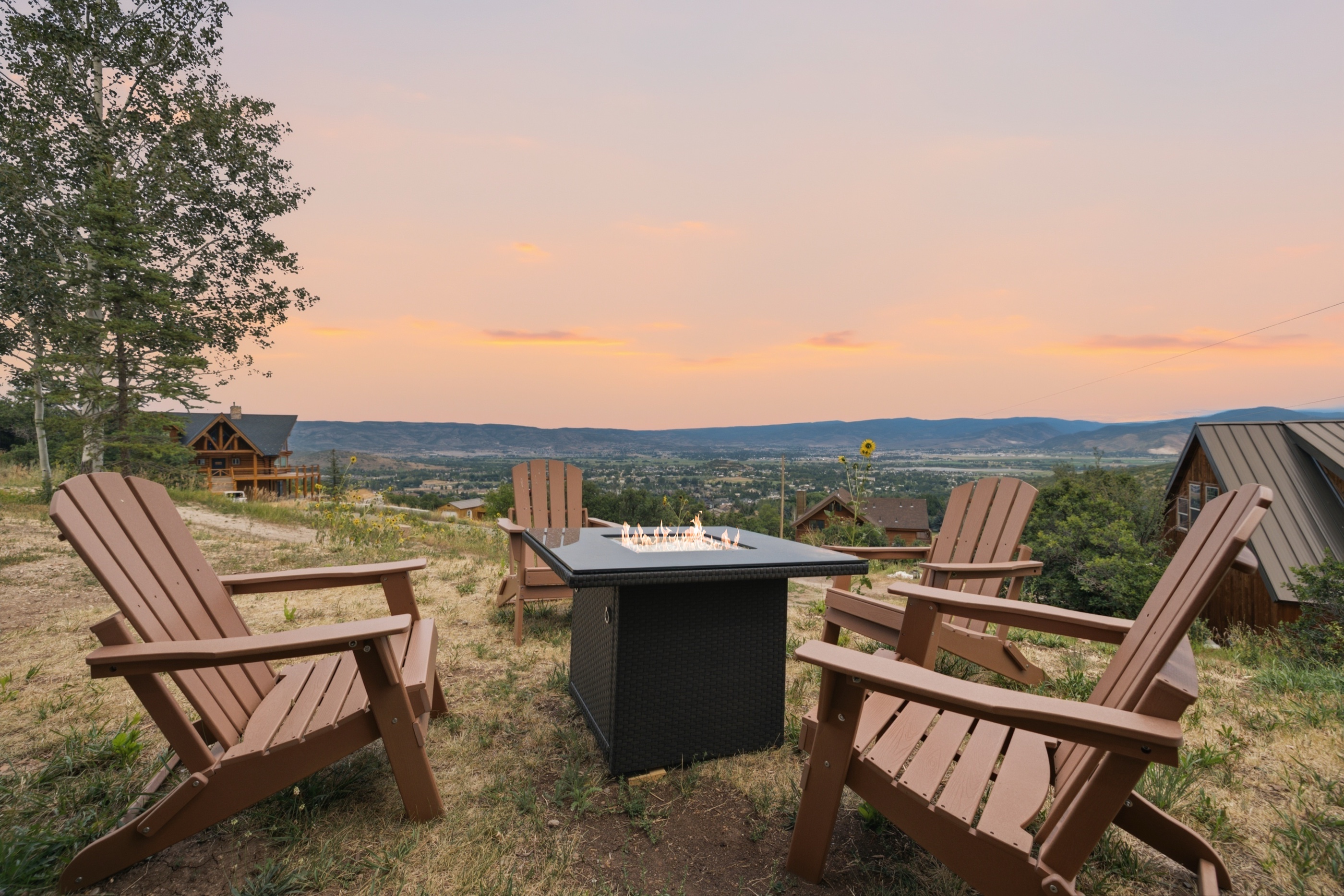 Adirondack chairs around a lit fire table at sunset, overlooking a Utah valley at a Vanik-managed property