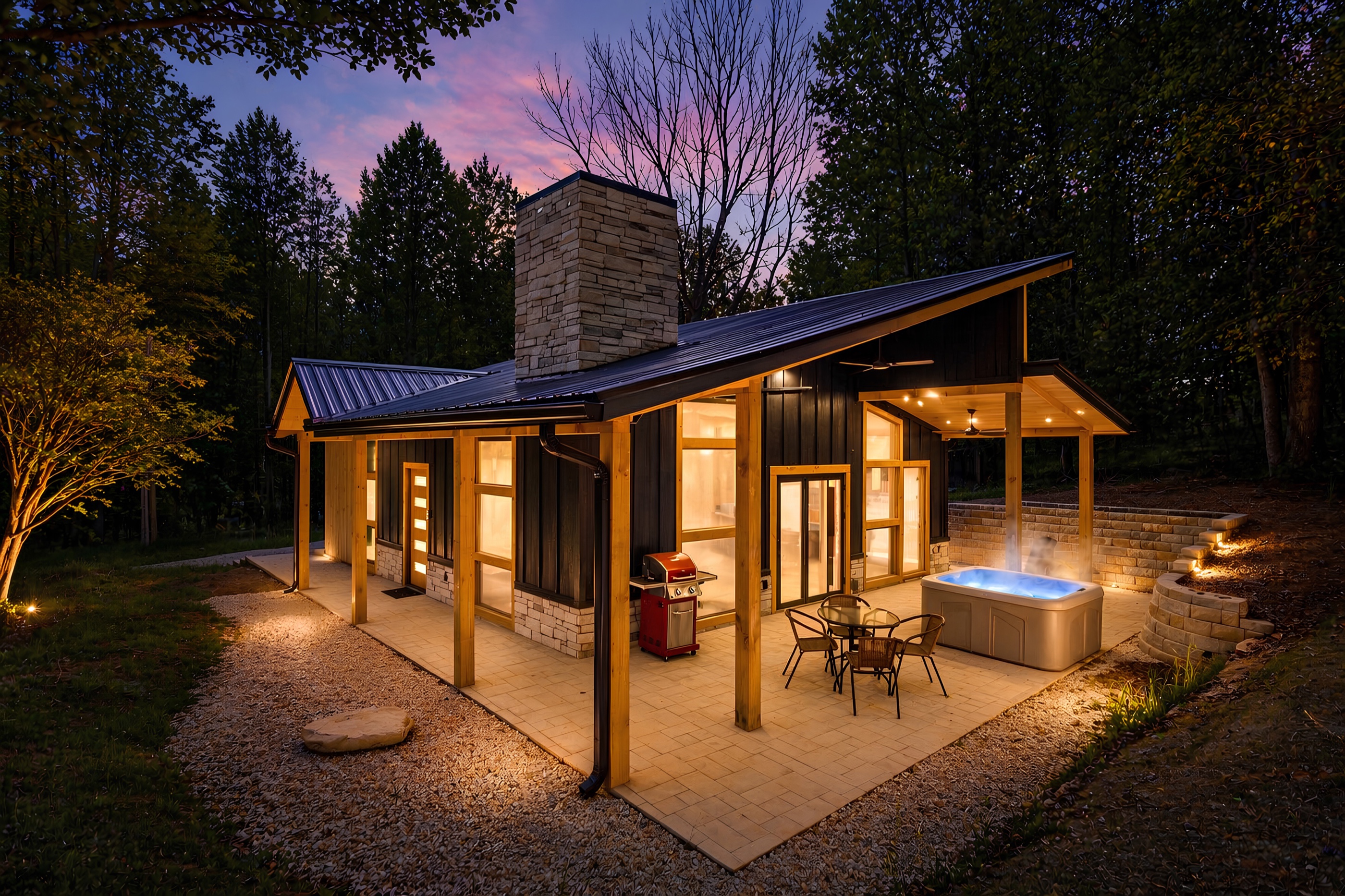 A modern cabin glowing at twilight — steaming hot tub, warm windows, and forest all around, at the Stone and Cedar Escape, a Vanik-managed property