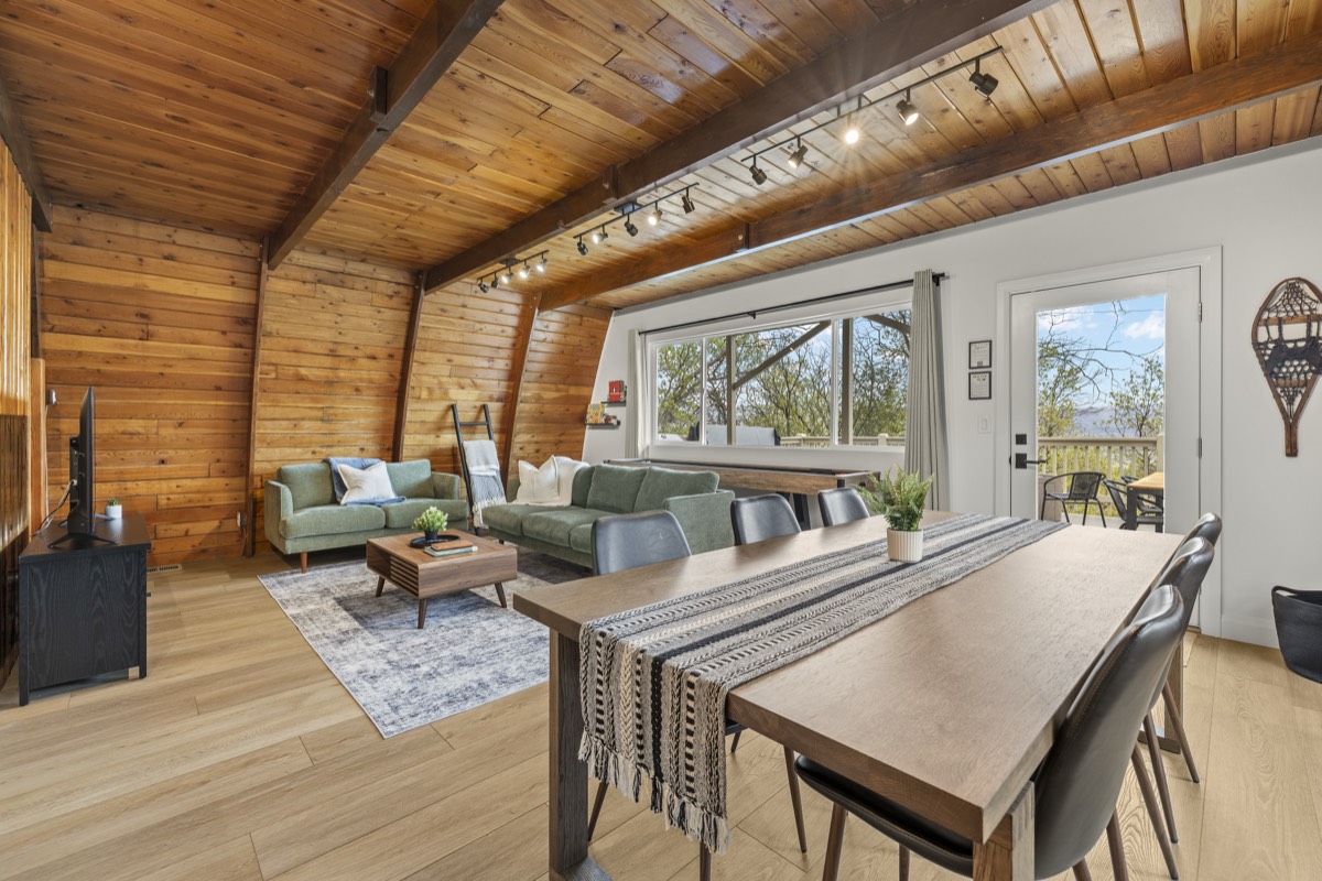 Warm wood-paneled A-frame cabin living room with green sofas